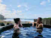 Couple in cliff top hot tub laughing with a sea view in the background