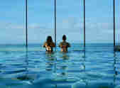 Two people stand looking out across the sea from the sea view pool in Swim Club at Watergate Bay