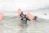 A surf instructor helps two young children push their boards over a wave in the sea off the north Cornwall coast