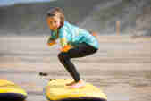 A child stands on a surf board on the sand