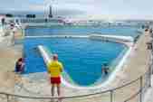 Jubilee Pool in Penzance - a lifeguard overlooks a blue curved outdoor swimming pool 