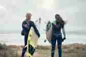 Two girls standing on the cliff overlooking the waves with surfboards in hand