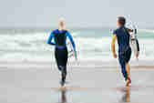 A couple in wetsuits running into the sea with surfboards