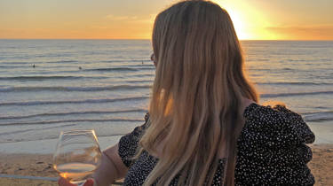  Anna Jones holds a glass of wine and looks out across the sea to the sunset