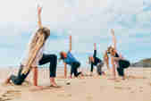 A yoga class taking place on the beach with the sea in the background