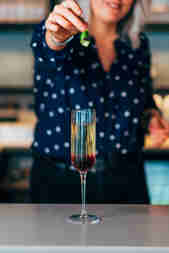 Lady holding lime twist over kir royale cocktail