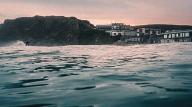 Watergate Bay hotel from the sea at dusk with a surfer in shot