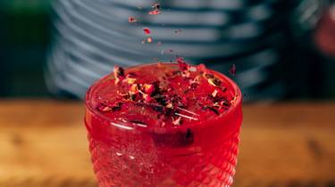 Blueberry and rose collins cocktail in a short glass with petals dusted on top