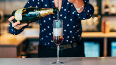 Bar tender pouring champagne into kir royale cocktail glass