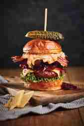 Large burger stacked with lettuce, meat, bacon, cheese and a pickle on top